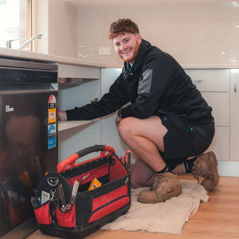 Grove plumber working on plumbing under a kitchen sink